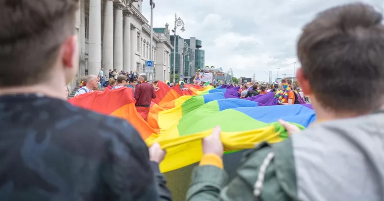 This article is about Ireland's ranking surrounding LGBTQ+ rights in Europe. The image shows Pride in Dublin, with people holding a large flag on the quays.