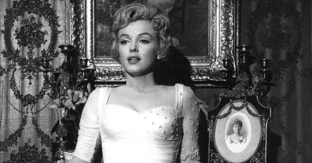 Black and white image of Marilyn Monroe, photographed from the stomach up, wearing a white dress.