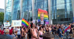 This article is about a 13-year-old boy charged under Russia's LGBT propaganda law. In the photo, People protesting in the streets carrying Pride flags and a sign with Putin's face on it.