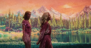 Still from sapphic slasher movie Teenage Sex And Death At Camp Miasma, with the two protagonist walking in front of a screen while covered in blood.