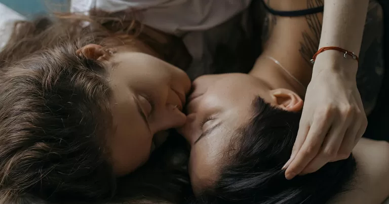 This article is about how LGBTQ+ people use sex for self-care. The image shows a close up of the faces of a queer couple embracing lying down.