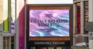 Image of a Trans+ History Week's campaign at Churchill Square. It shows a screen with water in the background, featuring the words "Change has never stood still".