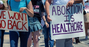 A sign reads "Abortion Is Healthcare". This article covers the three day abortion waiting period.
