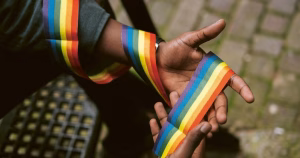 This article is about the International Protection Act 2026. In the photo, the hands of a person holding a fabric strip in the colours of the rainbow.
