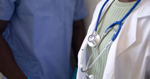 This article is about the government's new Policy and Oversight Group for Gender Healthcare in Ireland. The image shows the torsos of two medical professionals. The person on the left is dressed in blue scrubs, and the person on the right has a white overcoat on with a stethoscope around their neck.