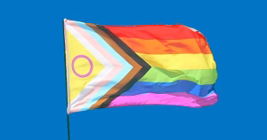 An image of the Pride progress flag flying with a blue sky in the background.