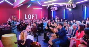 The Loft at Rascals Brewing Company. There is a crowd of people sitting down, while one person holds a mic and reads a speech.