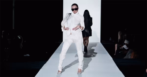Screenshot of Charli xcx from the SS26 music video. She wears an all white suit and black sunglasses on a white runway.
