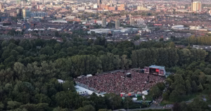 Birds eye view of Feile an Phobail. It shows a large crowd in an outdoor venue in a forest, with the city in the background.