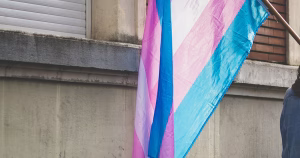 This article is about how embracing ones gender identity can lead to a happier life. The image shows a trans flag being carried through a street.