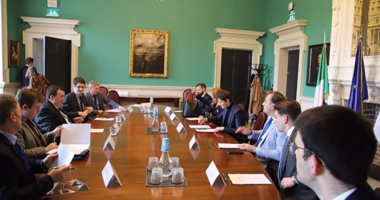 The article is about changes to Ireland's family reunification policies. The image shows the Chair of the Joint Committee sitting around a table in a room with green walls.