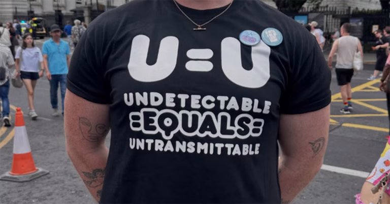 The torso of a person wearing a black HIV T-shirt with "U=U undetectable equals untransmittable" on it.