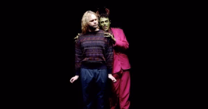 Still from the short film Demon Twink. The Demon is whispering over main character Dante's shoulder. The demon has green skinned, horns, sharp teeth and is wearing a pink suit. Dante is an older man with thinning blonde hair and a beard.