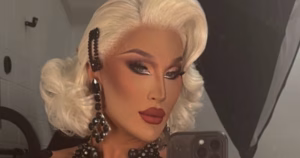 A mirror selfie of The Vivienne. She wears a blonde wig with a clip at the side.