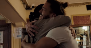 The article is about the Sexual Health Centre short film My Day Is The Same As Yours. The image depicts the protagonist Gabriel hugging his friend