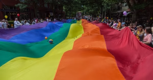This article is about Seattle adopting measures to protect polyamory, asexuality and pansexuality. In the photo, people carrying a massive Pride flag in the streets of Seattle.